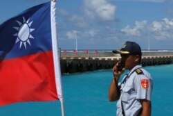 FILE - A member of the Taiwanese Coast Guard stands guard next to a Taiwanese flag on Itu Aba, which the Taiwanese call Taiping, at the South China Sea, Nov. 29, 2016.