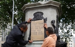 FILE - A banner is taped over the inscription on the pedestal of the toppled statue of Edward Colston in Bristol, England, June 8, 2020.