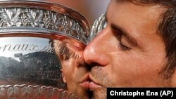 Novak Djokovic mencium trophy setelah menjuarai turnamen Perancis Terbuka di Roland Garros, Paris hari Minggu (5/6).