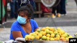 Archivo - Una mujer usa una máscara facial mientras espera clientes en un mercado en Tegucigalpa.