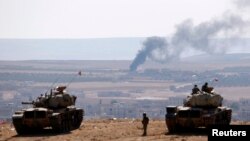 Tentara Kurdi dengan tank di sisi perbatasan Turki menyaksikan asap mengepul dari kota Kobani di Suriah (8/10). (Reuters/Umit Bektas)