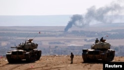 Turkish army tanks are seen on the Turkish side of the border as smoke rises from the Syrian town of Kobani Oct. 8, 2014.