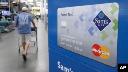 FILE - A customer walks past a sign promoting Sam's Club MasterCard credit cards at a Sam's Club store store in Bentonville, Ark., June 4, 2015.