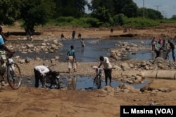 Residents of the heaviest-hit southern areas of Malawi struggle to cross the road, which is largely cut off by flooding brought by Cyclone Idai.