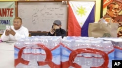 Terrence Valen, president of the National Alliance for Filipino Concerns, center, talks on the phone next to Joey Elacion as they sit behind bottles of water donated by Elacion for victims of Typhoon Haiyan, at the Filipino Community Center in San Francisco, Nov. 11, 2013. 