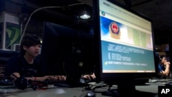 FILE - Computer users sit near a monitor display with a message from the Chinese police on proper online behavior, at an Internet cafe in Beijing, China, Aug. 19, 2013. 