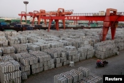 FILE - Workers ride through an aluminum ingots depot in Wuxi, Jiangsu province, China, Sept. 26, 2012.