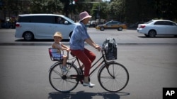 FILE - A boy rides on the back of a bicycle along a street in Beijing, June 1, 2018.