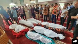 Kerabat dan para pelayat berdiri di samping jenazah lima anak keluarga Abu Dagga yang tewas dalam serangan udara Israel pada pemakaman mereka di Khan Younis, Jalur Gaza selatan, Sabtu, 7 Oktober 2023. (AP /Yousef Masoud)