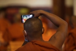 A Buddhist monk takes photographs with a mobile phone as his gathers for chanting in a pagoda in Phnom Penh, Cambodia, Monday, Mar. 23, 2020. Buddhist pagodas in Cambodia on Monday offered prayer, chanting and strikes of a gong and drum in attempts to chase away the new coronavirus. (AP Photo/Heng Sinith)