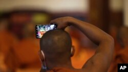 A Buddhist monk takes photographs with a mobile phone as they gather for chanting in a pagoda in Phnom Penh, Cambodia, Monday, Mar. 23, 2020. (AP Photo)