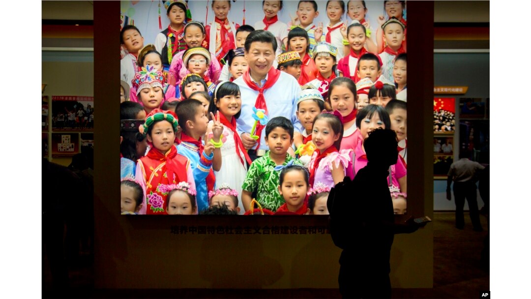 Seorang pengunjung berjalan melewati foto Presiden China Xi Jinping dikelilingi oleh anak-anak di sebuah pameran di Beijing pada 2017. (Foto: AP)