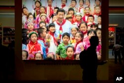 Seorang pengunjung berjalan melewati foto Presiden China Xi Jinping dikelilingi oleh anak-anak di sebuah pameran di Beijing pada 2017. (Foto: AP)