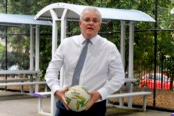 PM Australia Scott Morrison memegang bola saat meninjau sekolah di Sydney, 8 Desember 2021.