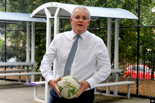 PM Australia Scott Morrison memegang bola saat meninjau sekolah di Sydney, 8 Desember 2021.