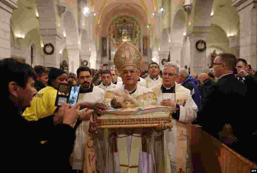 The Latin Patriarch of Jerusalem Fouad Twal (C) carries a statuette of baby Jesus during a Christmas midnight mass at the Church of the Nativity believed to be the birthplace of Jesus Christ, in the West Bank biblical town of Bethlehem, Dec. 25, 2014.