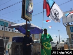 Tanzanians wearing ruling party CCM promotional clothing stand underneath opposition party Chadema flag in Dar es Salaam, Oct. 23, 2015. (Photo: Jill Craig / VOA)