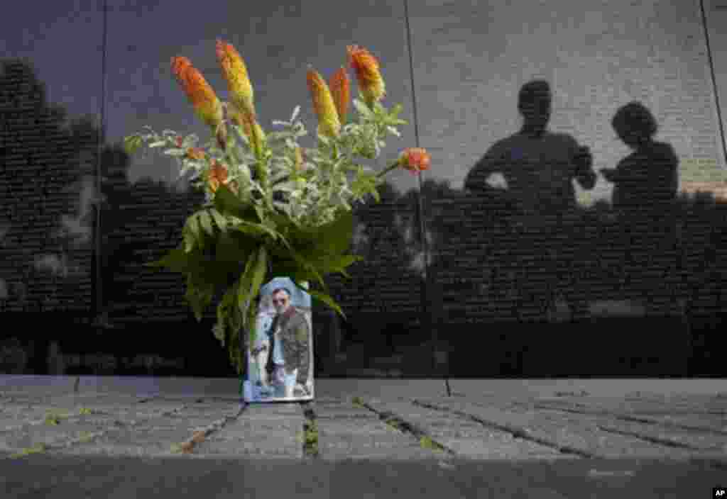 A bouquet of flowers in a can wrapped in a photo is seen as visitors pause along the Vietnam Veterans Memorial Wall on the 50th anniversary of the Vietnam War, Monday, May 28, 2012, on Memorial Day in Washington. (AP Photo/Carolyn Kaster)