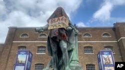 The statue of Robert Milligan, a noted West Indian merchant, slaveholder and founder of London's global trade hub, West India Docks, stands covered in a sack-cloth and sign reading Black Lives Matter, outside the Museum of London Docklands, June 9, 2020.