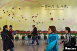 FILE - Visitors walk past a wall with a map showing the species of peony in Belt and Road Initiative (BRI) countries, at horticultural exhibition Beijing Expo 2019, in Beijing, China, April 29, 2019.