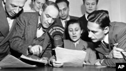 FILE - A group of State Department announcers huddle around the microphone after the initial shortwave broadcast in Russian to Russia from New York City, Feb. 17, 1947.