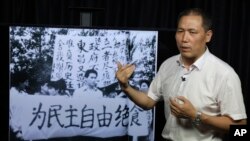 In this May 22, 2019, photo, Pu Zhiqiang recalls his experience near a photo which showed him taking part in the 1989 pro-democracy protest near a banner which reads "Hunger strike for democracy" during an interview in Beijing. (AP Photo/Ng Han Guan)