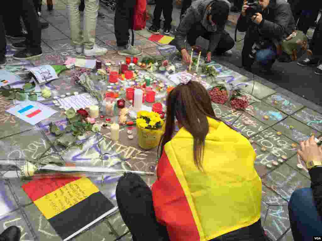Woman draped in Belgian flag places memento at makeshift memorial in honor of terror bombing victims in Brussels, Belgium, March 23, 2016. (N. Pourebrahim / VOA )