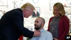 President Donald Trump awards a Purple Heart to U.S. Army Sgt. 1st Class Alvaro Barrientos, with his wife, Tammy Barrientos, right, at Walter Reed National Military Medical Center, in Bethesda, Md., April 22, 2017.