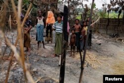 A family stands beside remains of a market, which was set on fire in Rohingya village, outside Maungdaw in Rakhine state, Myanmar, Oct. 27, 2016.
