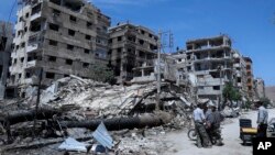 시리아 정부군의 화학무기 공격을 받은 곳으로 여겨지는 시리아 동구타 두마에서 시민들이 폐허가 된 건물 앞에 서 있다. 
