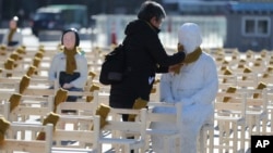 A woman puts a scarf on a statue of a comfort woman sitting in a installation of empty chairs symbolizing the victims in Seoul, South Korea, Dec. 27, 2017. 