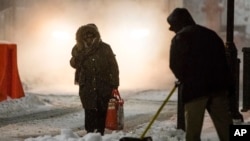 在宾州费城，一名女士小心翼翼地走在人行道上，工人在一旁忙着产出冰雪。（2017年3月14日）