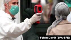 A health worker measures the temperature of a woman outside a hospital in Sarajevo, May 26, 2020