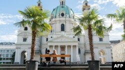 FILE - People sit on a bench in front of the Karlskirche, or St. Charles' church, on the Karlsplatz square in the Austrian capital, Vienna, Oct. 5, 2017.