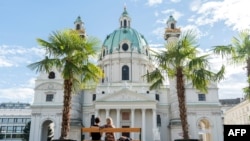 FILE - People sit on a bench in front of the Karlskirche, or St. Charles' church, on the Karlsplatz square in the Austrian capital, Vienna, Oct. 5, 2017.