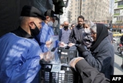 People queue in line to receive packages for precautions against COVID-19 coronavirus disease outside Meydane Valiasr metro station in Tehran, March 15, 2020.