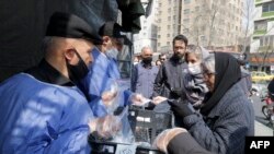 People queue in line to receive packages for precautions against COVID-19 coronavirus disease from a booth outside Meydane Valiasr metro station in Tehran, March 15, 2020.