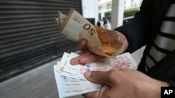 FILE —A man holds Algerian and European, top, bank notes February 9, 2024 in Algiers. In Algeria, people rely on foreign currencies to buy imported items in short supply or finance their children's educations abroad.