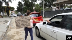 La migrante venezolana Verónica Hernández, de 20 años, embarazada de ocho meses, con un cartel con un mensaje escrito a mano pidiendo comida o dinero, extiende su mano para recibir una limosna de un conductor, en Bogotá, el martes 9 de febrero.
