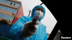 FILE - A medical worker holds a thermometer to check a passenger's temperature at a checkpoint as the country is hit by an outbreak of the coronavirus in Susong County, Anhui province, China, Feb. 6, 2020.