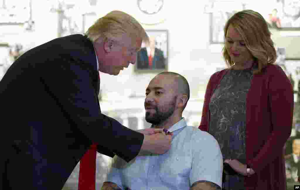 Presidente Donald Trump coloca laço do Coração Lilás (Purple Heart) na gola do 1&ordm; Sargento americano Alvaro Barrientos, e galardoa com o mesmo laçoi a sua mulher Tammy Barrientos,(à direita) no Walter Reed National Military Medical Center, em Bethesda, Maryland. Abril &nbsp;22, 2017.