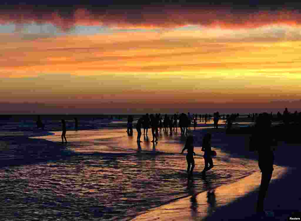 Pessoas caminham na praia aproveitando o pôr-do-sol em Valeria del Mar, Argentina, Fev. 21, 2017.