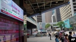 People wearing face mask walk past a bank's electronic board showing the Hong Kong share index at Hong Kong Stock Exchange, June 23, 2020. 