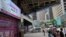 People wearing face mask walk past a bank's electronic board showing the Hong Kong share index at Hong Kong Stock Exchange, June 23, 2020. 