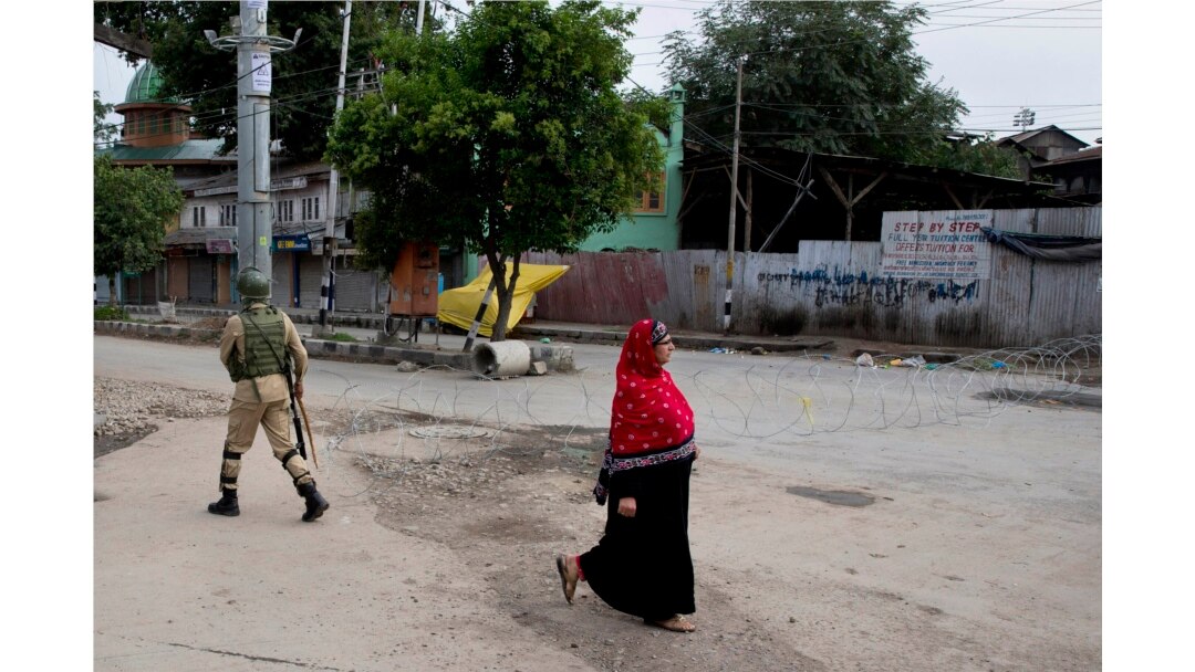 A woman walks past an Indian paramilitary soldier who prepares to block a road with barbed wires during security lockdown in Srinagar, Indian-controlled Kashmir, Aug. 18, 2019.