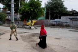 A woman walks past an Indian paramilitary soldier who prepares to block a road with barbed wires during security lockdown in Srinagar, Indian-controlled Kashmir, Aug. 18, 2019.