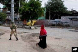 A woman walks past an Indian paramilitary soldier who prepares to block a road with barbed wires during security lockdown in Srinagar, Indian-controlled Kashmir, Aug. 18, 2019.