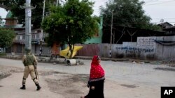 A woman walks past an Indian paramilitary soldier who prepares to block a road with barbed wires during security lockdown in Srinagar, Indian-controlled Kashmir, Aug. 18, 2019. 