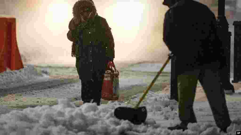 A woman makes her way in the street as a worker clears snow from a sidewalk during a winter storm in Philadelphia, Pennsylvania, March 14, 2017