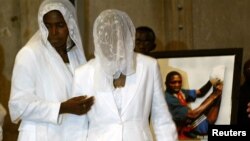 FILE - The wife, Marie-Louise Foe (C), and mother (L), of the late Cameroon player Marc-Vivien Foe, walk past his picture during his funeral ceremony.